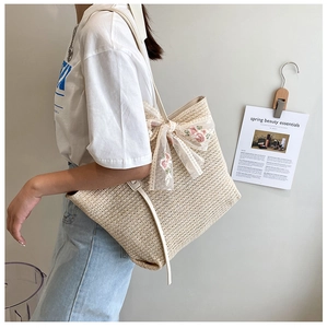 Detail of straw tote bag featuring delicate lace bow with pink floral embroidery