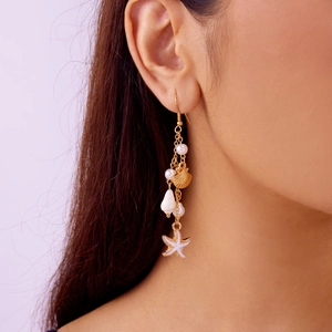 Detail shot of long ocean style earrings with gold starfish and pearl tassels on a model