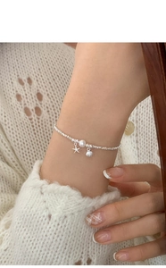 Detailed shot of starfish and shell charms on a silver beaded pearl bracelet