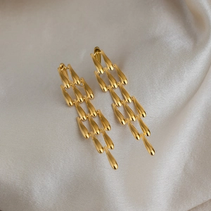 Boucles d'oreilles dorées en gouttes d'acier inoxydable sur fond de soie douce