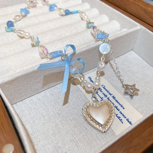 Détail du collier de perles avec pendentif cœur bleu et nœud dans une boîte à bijoux