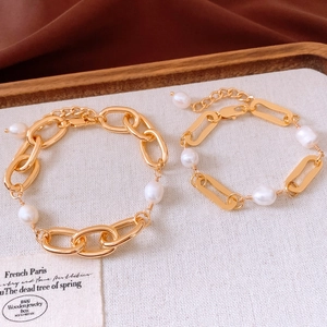 Close-up of 18k gold plated chain bracelets with baroque pearls on a wooden tray