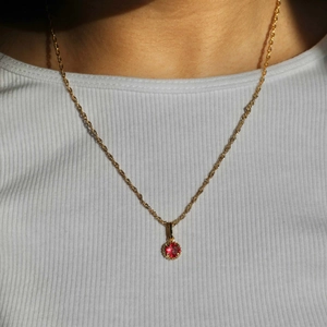 Golden stainless steel necklace with a red round birthstone pendant worn on neck