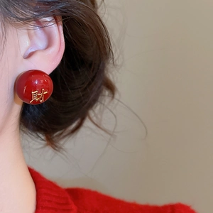 Vue détaillée de boucles d'oreilles perles rouges avec caractère chinois doré gravé