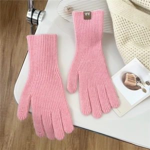 Detail of pink knitted glove with ribbed cuff and brown D.D leather patch on white surface