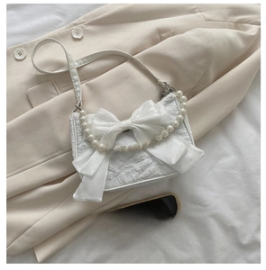 Detail of white ruffled bag featuring a large silk bow and elegant pearl carry handle