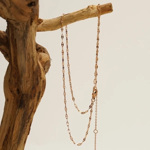 Minimalist rose gold stainless steel necklace draped over a rustic wooden branch