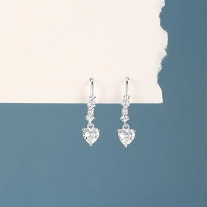 Macro detail of silver S925 earrings with heart-shaped zircon pendants and diamond accents