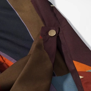 Close-up of geometric satin shirt fabric with golden metal button and colorful pattern