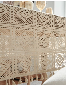 Detailed close-up of beige crochet tablecloth with diamond patterns and fringe edges