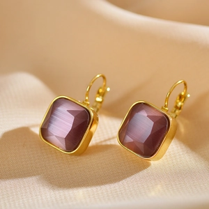 Macro detail of gold plated square earrings with purple stones on silk fabric