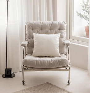 Detail of a beige upholstered armchair with button tufting and white throw pillow
