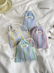 Macro detail of pleated striped drawstring pouches in assorted colors on a soft bed
