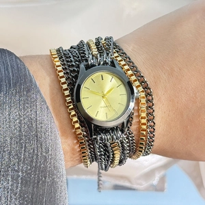 Detail of a gold quartz watch featuring a layered black and gold chain wrap strap