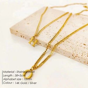 Detailed view of 14K gold plated stainless steel initial letter necklaces displayed on stone