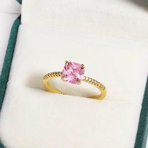 Macro view of gold ring with square pink stone and white diamonds on velvet box