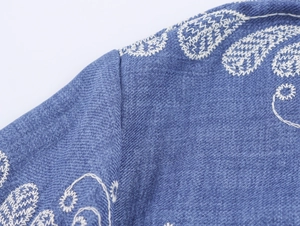 Détail de broderies florales blanches sur l'épaule en denim bleu d'une robe à revers