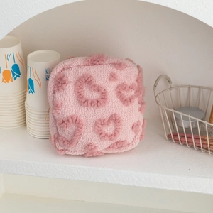 Détail d'une trousse de toilette en peluche rose avec motifs de cœur et zip doré