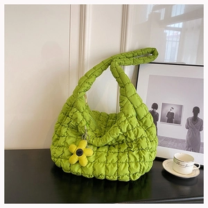 Detail of green quilted cloud tote bag with floral charm on a minimalist desk setup