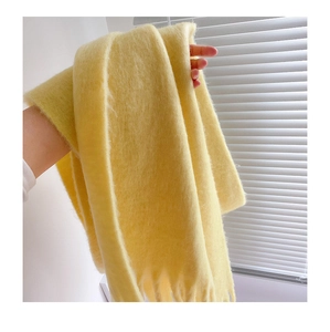 Close-up of soft yellow mohair scarf texture with tassels held by hand for warmth