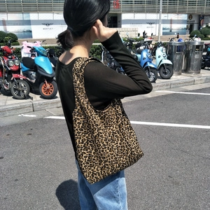 Vista esterna di una grande borsa tote in tela con stampa leopardata portata a spalla da modella