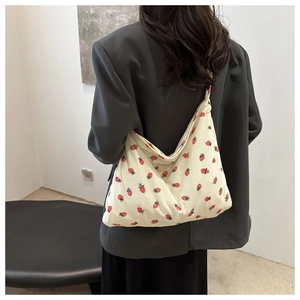 Detail of off-white corduroy tote bag with red strawberry print worn by a model