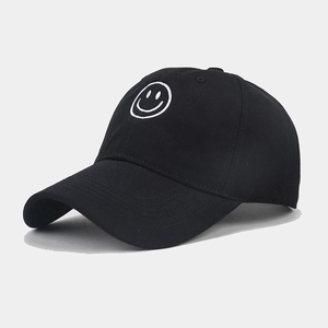 Close-up of a black baseball cap featuring a white embroidered smiley face on the front