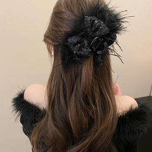 Detail of a large black sequin bow hair claw with feathers worn on long wavy hair