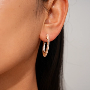 Close-up of geometric C-shaped silver earrings with wavy texture on a female model