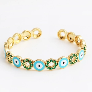 Detail view of golden evil eye bangle featuring blue enamel and green zircon inlay
