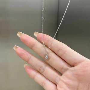 Macro shot of silver cross pendant with a round prong-set gemstone on a fine chain