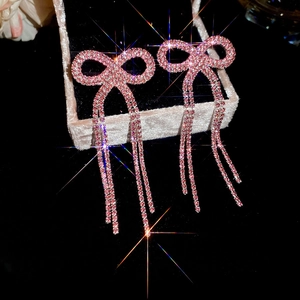 Macro view of pink bow earrings with rhinestone tassels on a pink jewelry box display