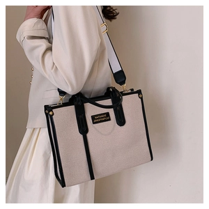 Detail view of canvas tote bag with black leather handles and gold metal accents