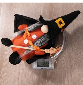 Dettaglio del peluche gnomo di Halloween con cappello da strega e scopa su una bilancia
