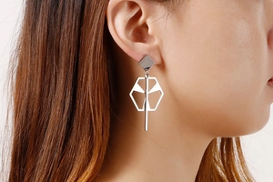 Macro detail of geometric hollow silver drop earrings worn on ear showing long modern design