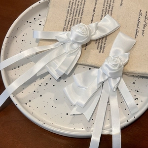 Detail of white satin bow hair clips with handmade roses and silky flowing tassels