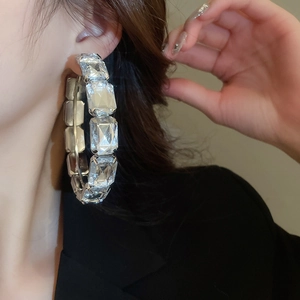 Close-up of large square crystal-encrusted silver hoop earrings worn by a model