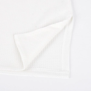 Close-up of white waffle knit fabric texture and high-quality hem slit detail on the dress