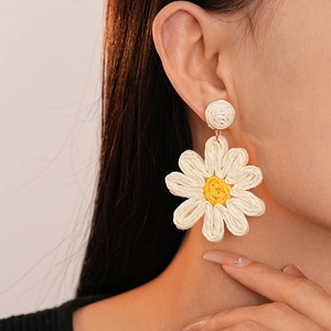 Close-up of hand-woven white flower earrings with yellow stamen worn by a model