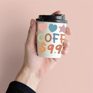 Close-up of hand holding a white coffee cup with colorful COFF stickers and star patterns