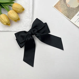 Detail of a large black satin bow hair clip with long ribbons on a white background
