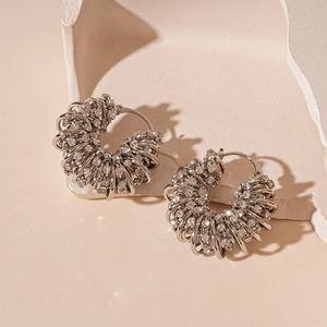 Détail de boucles d'oreilles argentées en U avec strass sur fond de pierre neutre