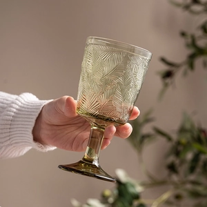Green embossed glass goblet with leaf patterns held against a natural soft background