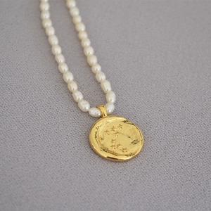 Macro shot of gold coin pendant with star engraving on white freshwater pearl necklace