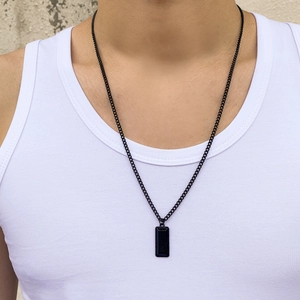 Close-up of a men's black rectangle geometric pendant necklace on a textured background