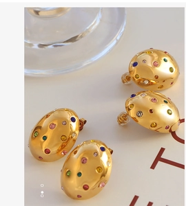 Close-up of gold oval stud earrings with colorful zircon inlay and polished metal finish