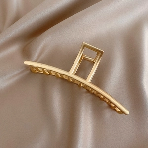 Macro detail of matte gold metal hair claw clip on champagne silk background