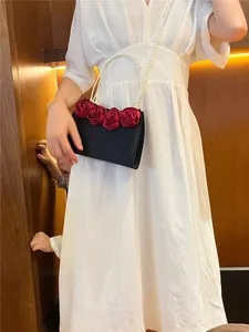 Detail view of a black evening bag with red satin roses and a faux pearl handle