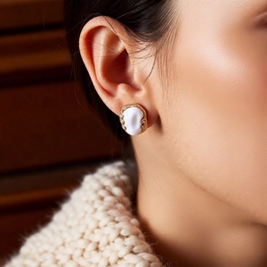 Detailed view of vintage gold-trimmed oval earrings on a model wearing a beige sweater