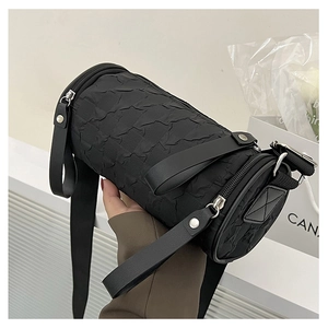 Detail of black cylindrical crossbody bag with pleated texture and silver hardware